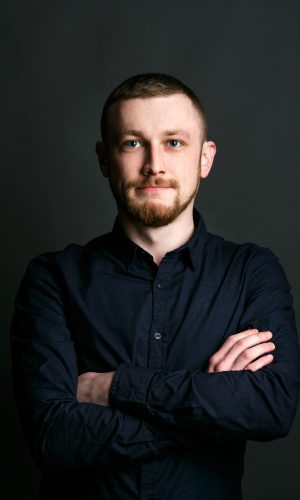 Dark blonde bearded man crosses his hands on chest posing in black shirt